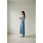 Side view of a woman wearing pale-blue boots and a blue midi dress while holding a cup.
