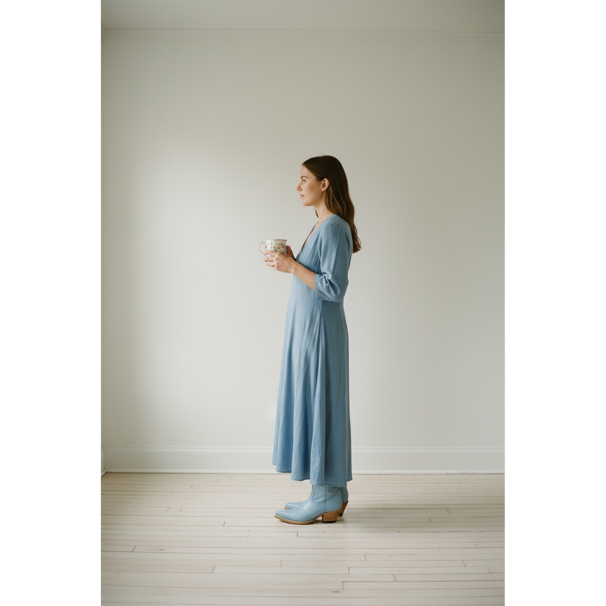 Side view of a woman wearing pale-blue boots and a blue midi dress while holding a cup.