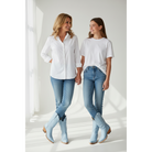 Two women wearing pale-blue boots with white tops and jeans beside a window.