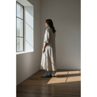 Woman wearing pale-blue boots with a light midi dress, standing beside a window.