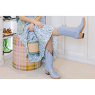 Woman sitting on a colorful stool wearing light blue boots in a room with white walls and wooden floor.