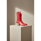 Red midi boot on a tall square pedestal in a sunlit room