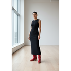 Woman in a black dress wearing red boots beside tall windows
