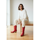 Woman in a white sweater and beige trousers wearing red boots while seated on a bench