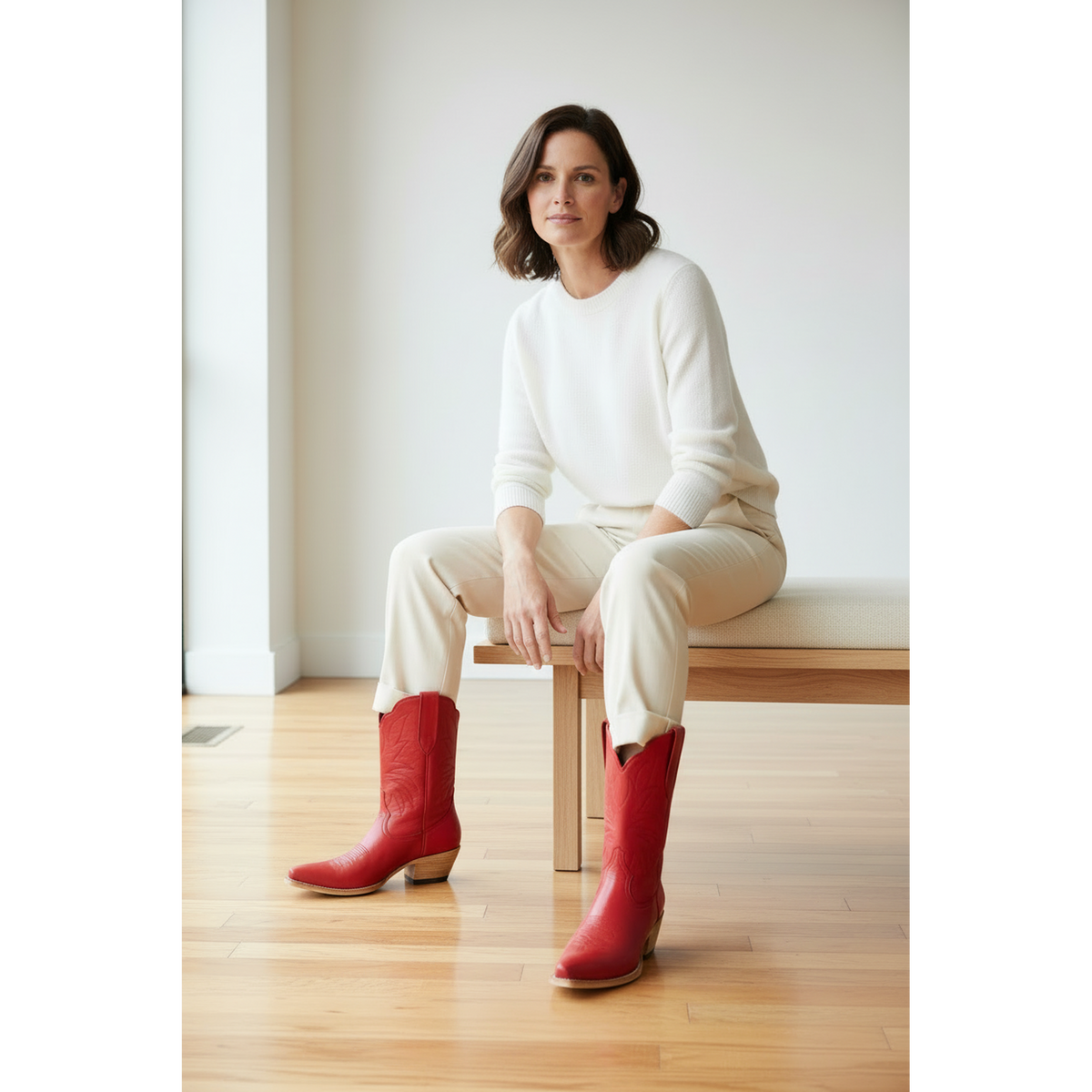 Woman in a white sweater and beige trousers wearing red boots while seated on a bench